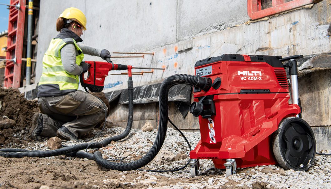 Woman using red Hilti Hammer drill connected with dust extractor.